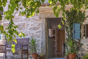 Un edificio de piedra con un banco de madera, plantas en macetas y una puerta de acceso.