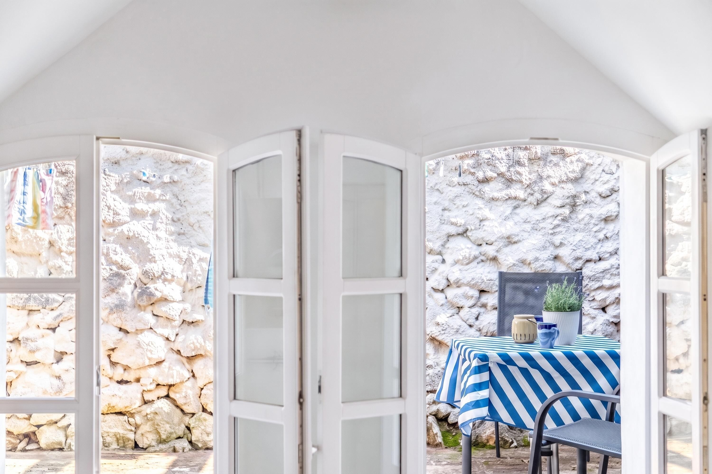 A room with a stone wall, a table with a striped tablecloth, and a chair.