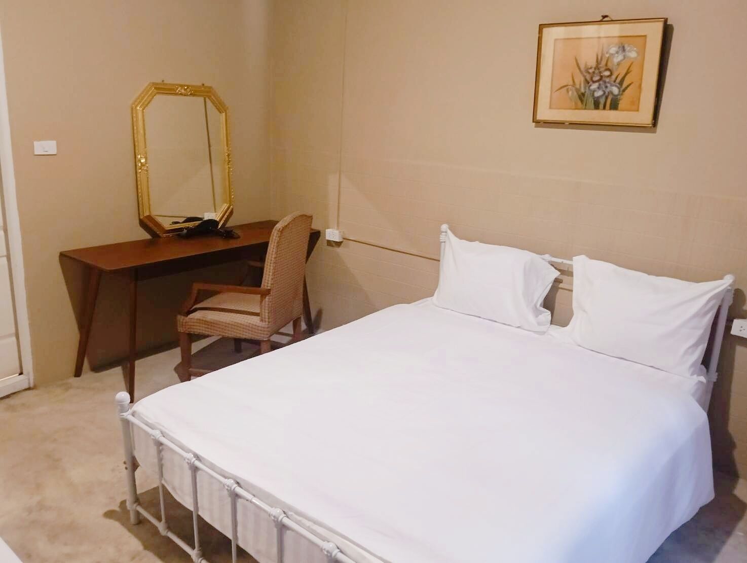 A bedroom with a bed, a desk, a chair, a mirror, and a framed picture on the wall.
