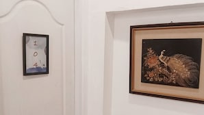 En hvid dør med nummer '104' i en ramme og et billede af en påfugl på væggen.