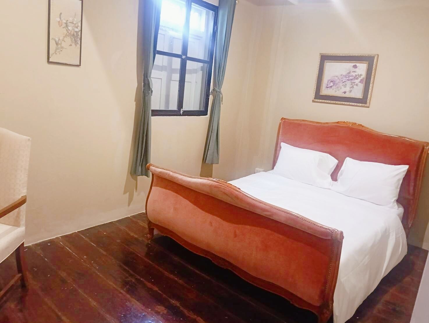 A bedroom with a wooden bed, a window with curtains, and two framed pictures on the walls.
