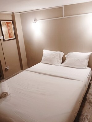 Ein Hotelzimmer mit einem großen Bett, zwei Kissen, einer Wandleuchte und einem gerahmten Bild an der Wand.