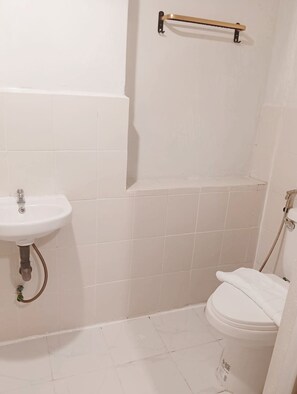 Ein kleines Badezimmer mit weißen Fliesen, einem Waschbecken, einer Toilette und einer Duschkabine.