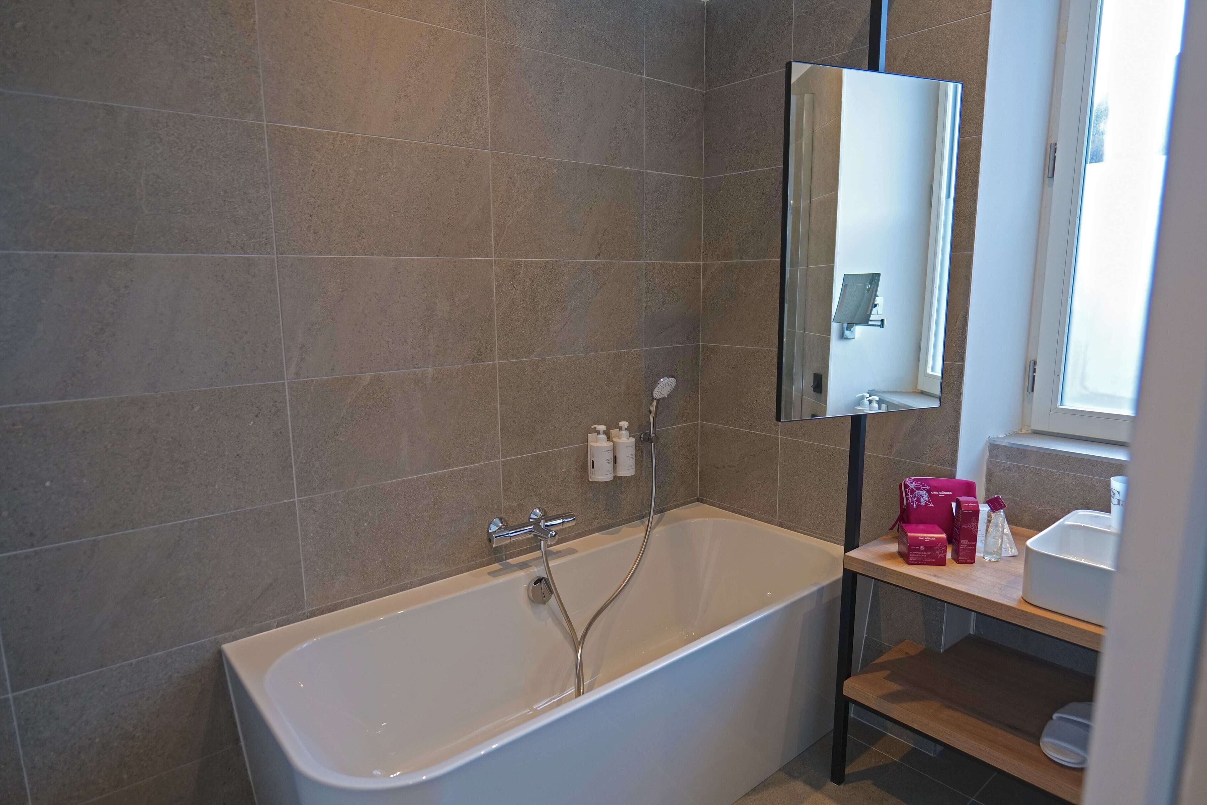 A modern bathroom with a freestanding bathtub, a mirror, and a shelf with toiletries.