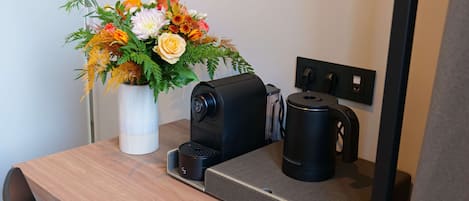 A wooden table with a coffee maker, a black mug, and a white vase with flowers.