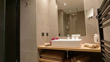 A modern bathroom with a large mirror, a sink, and neatly folded towels on shelves.