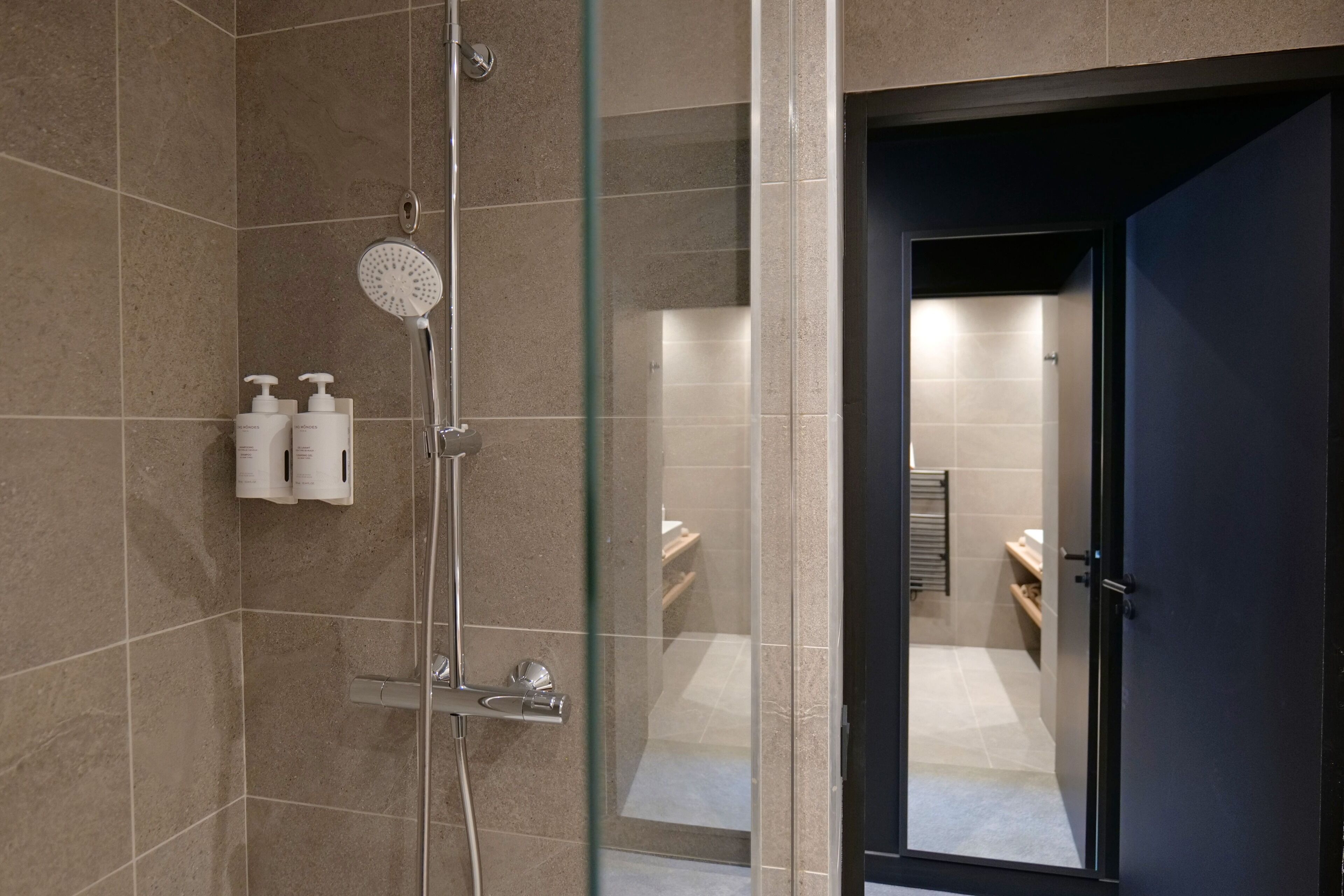 A modern bathroom with a glass-enclosed shower, beige tiles, and a dark door.