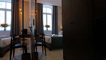 A hotel room with a bed, a desk with chairs, a vase with flowers, and a window with curtains.
