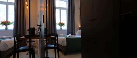 Et hotelværelse med en seng, et skrivebord med stole, en vase med blomster og et vindue med gardiner.