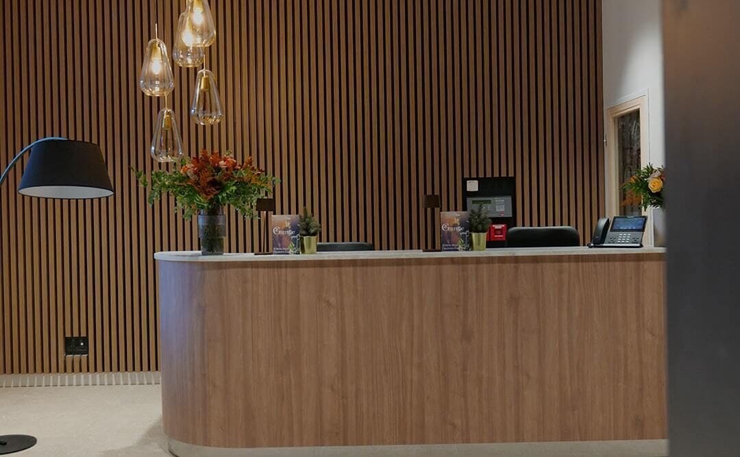 A reception desk with a wooden finish, a black desk lamp, and a vase with flowers.