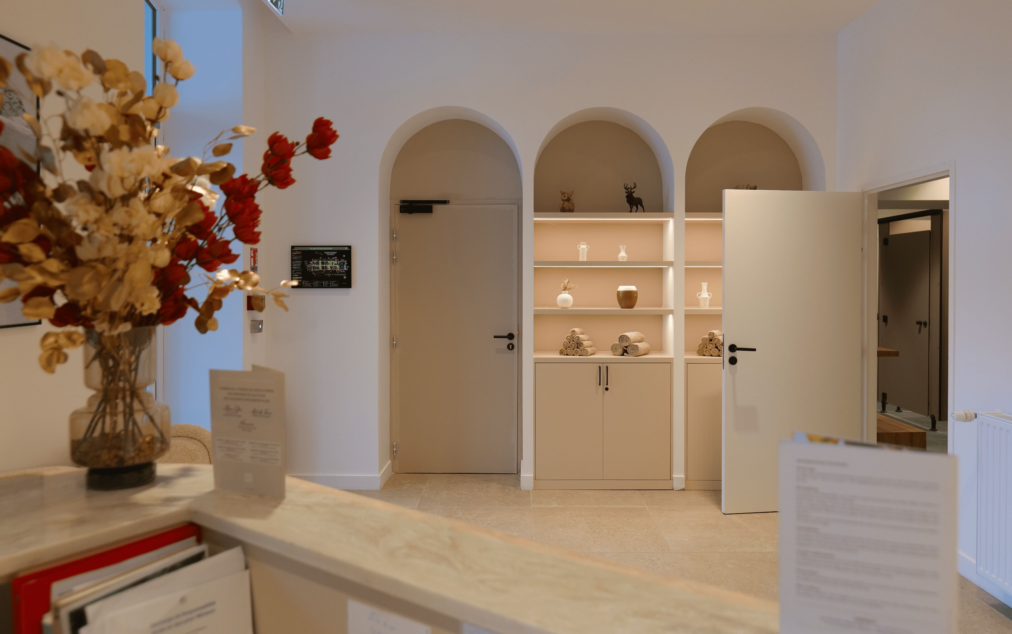 Eine Hotelhalle mit einer Rezeption, einem Blumenstrauß, einem Schwarzwert und einem Empfangsbereich mit rundbogigen Durchgängen zu den Zimmern.