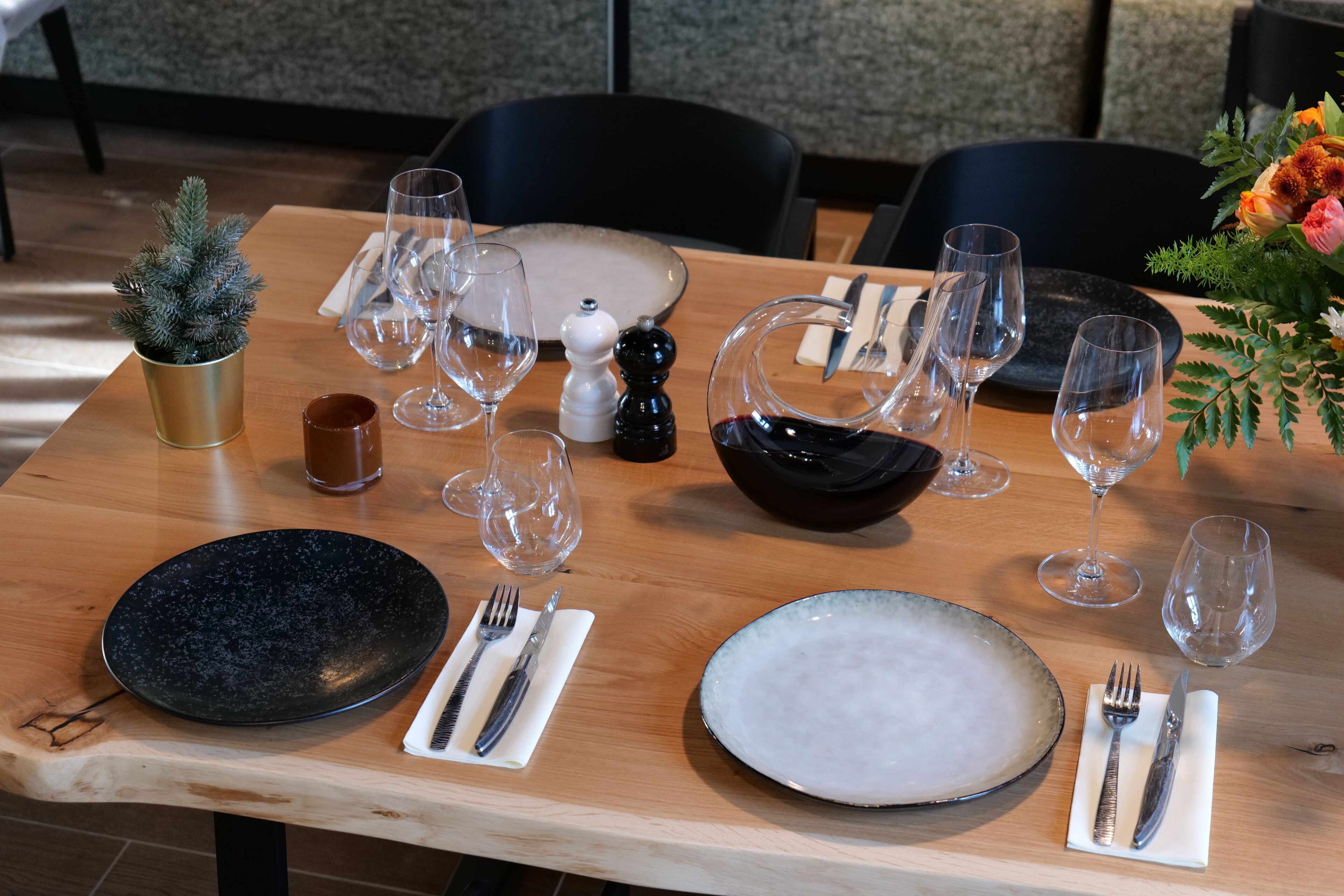 Una mesa de comedor dispuesta con platos, vasos, cubiertos y una pequeña planta en maceta.