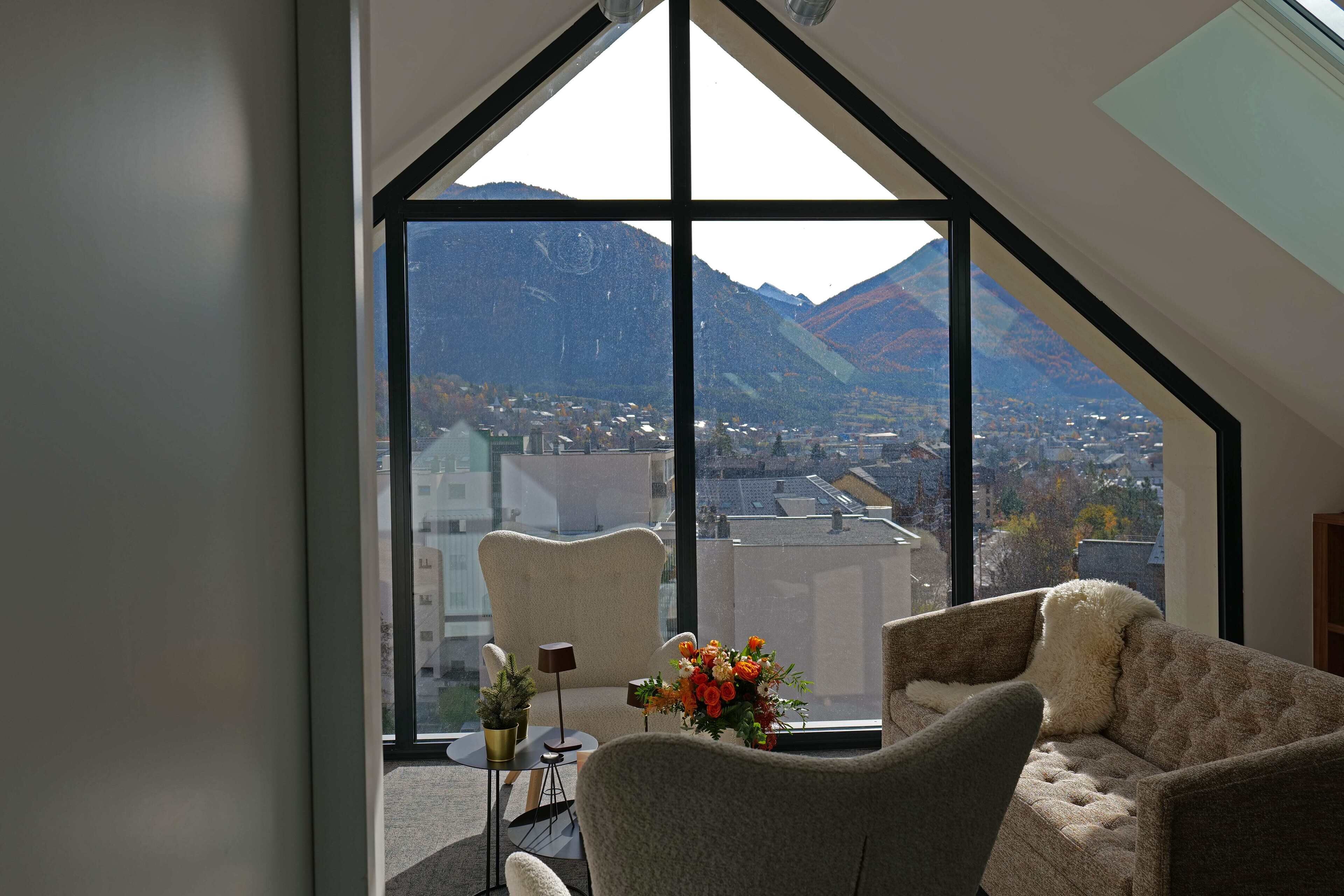 Une chambre moderne dotée d’une grande fenêtre offrant une vue sur les montagnes et le paysage urbain.