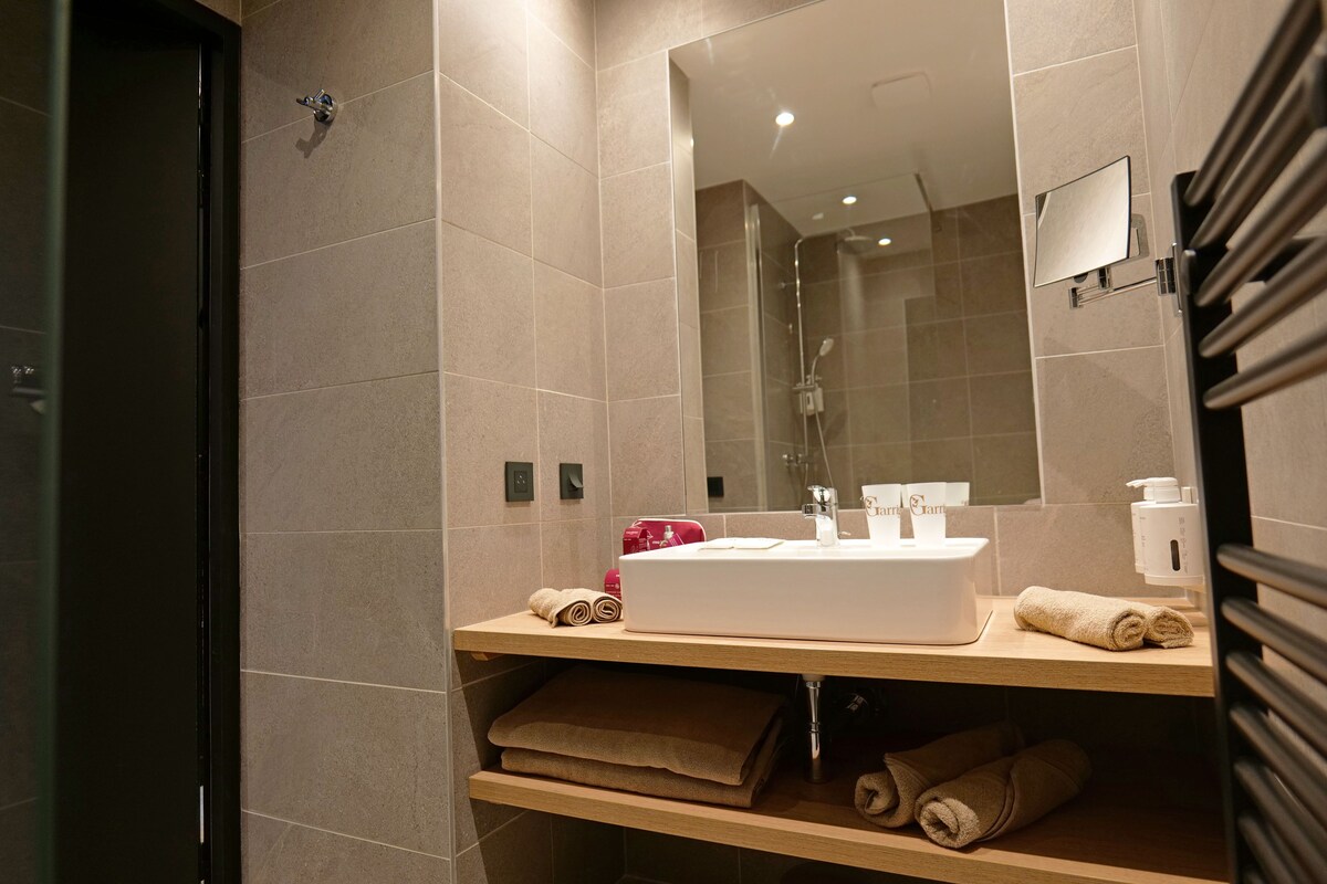 Un baño moderno con un espejo grande, un lavabo y toallas ordenadas en estantes.