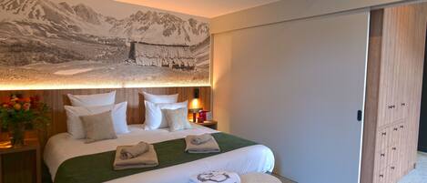 Habitación de hotel con una cama grande, un edredón verde y un mural con paisaje de montaña en la pared.