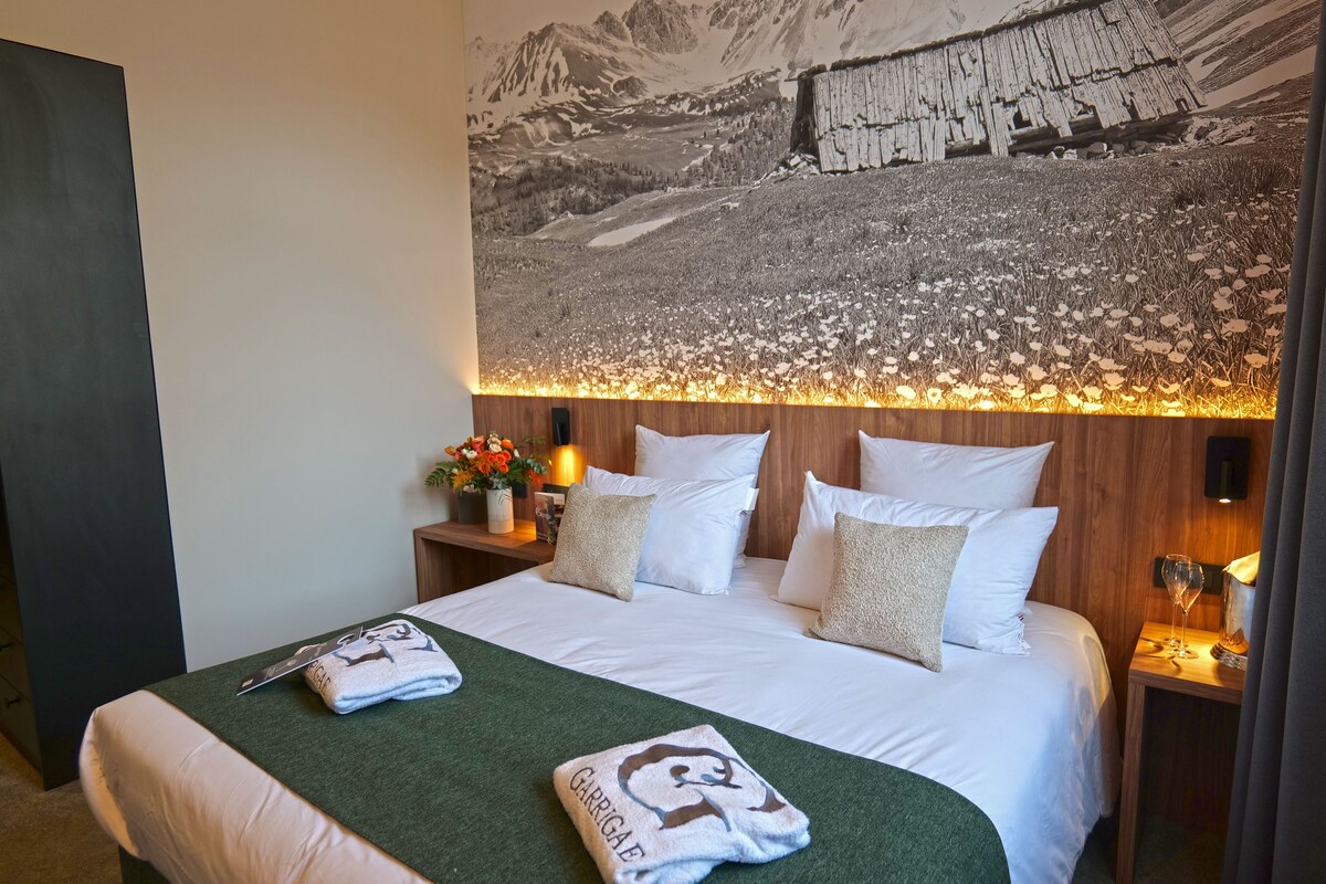 A hotel room with a bed, a nightstand with a lamp, a wall-mounted painting, and a window.