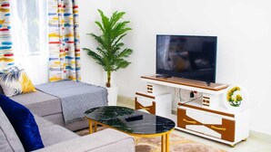 A living room with a sofa, a coffee table, a TV, and a plant. - Fully furnished onebedroom in Mombasa Bamburi Vescone1 estate (Mombasa)