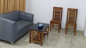 Un salon avec un canapé gris, deux chaises en bois, une petite table en bois et un ventilateur de plafond.