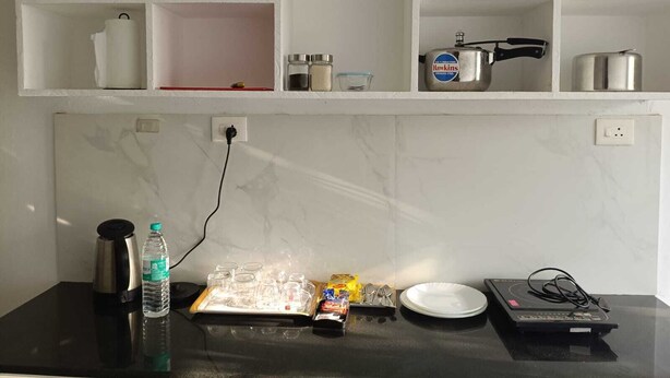 Une cuisine avec des meubles blancs, un pare-feu en marbre et un plan de travail sur lequel on trouve une bouilloire, une bouteille d’eau, des bocaux et un radiateur portatif.