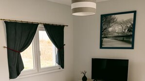 Un soggiorno moderno con un divano blu, un tavolino da caffè beige, una TV su un mobile bianco e un quadro appeso al muro.