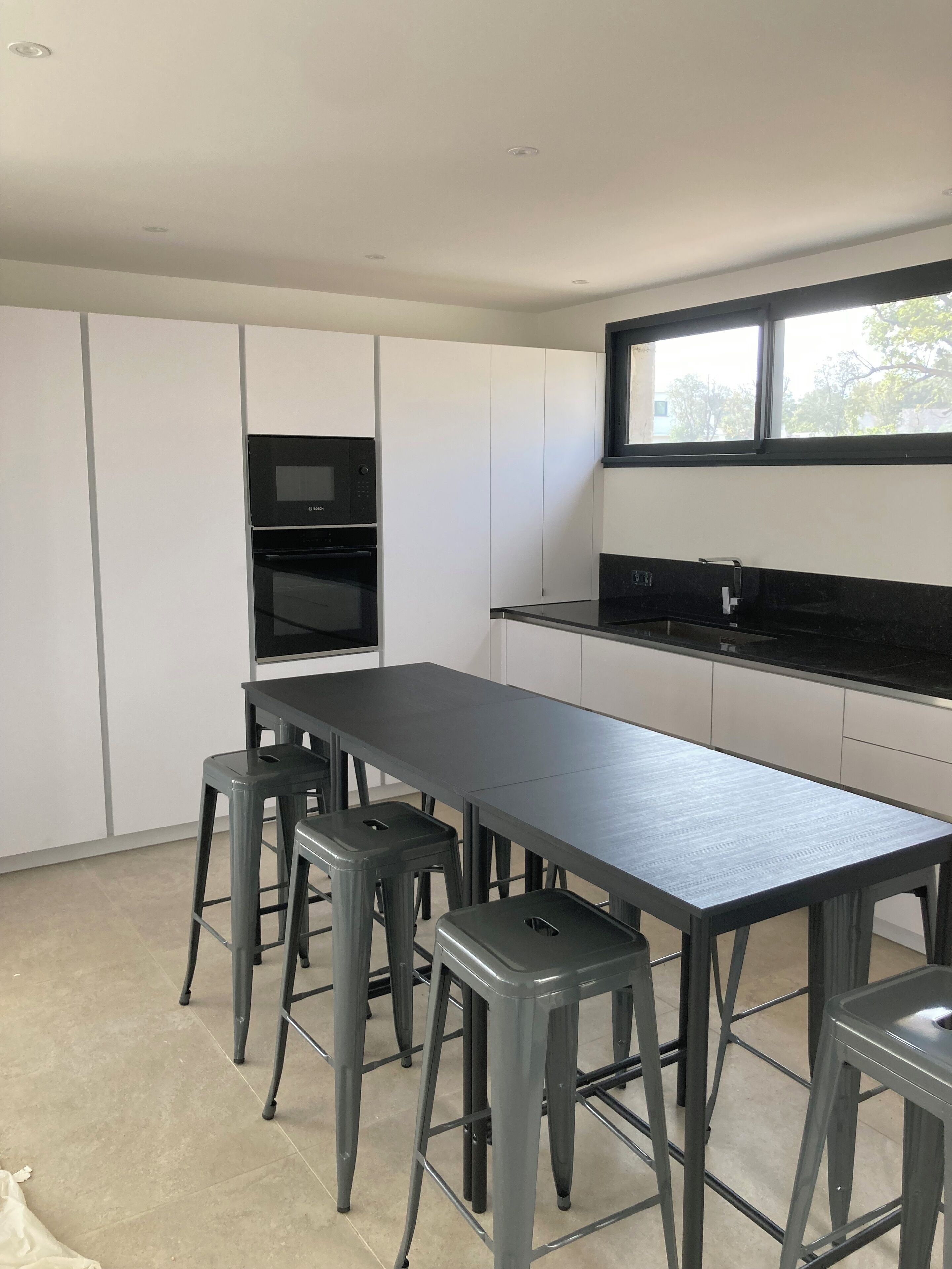 A modern kitchen with a long countertop, built-in appliances, and bar stools.