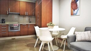 A modern kitchen with wooden cabinets, a built-in oven, and a dining area with white chairs and a table. - Desconectaengalicia Castiñeiros (Sanxenxo)