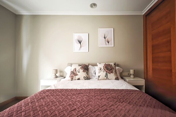 Une chambre à coucher avec un lit, deux tables de chevet, une porte en bois et deux tableaux accrochés au mur.