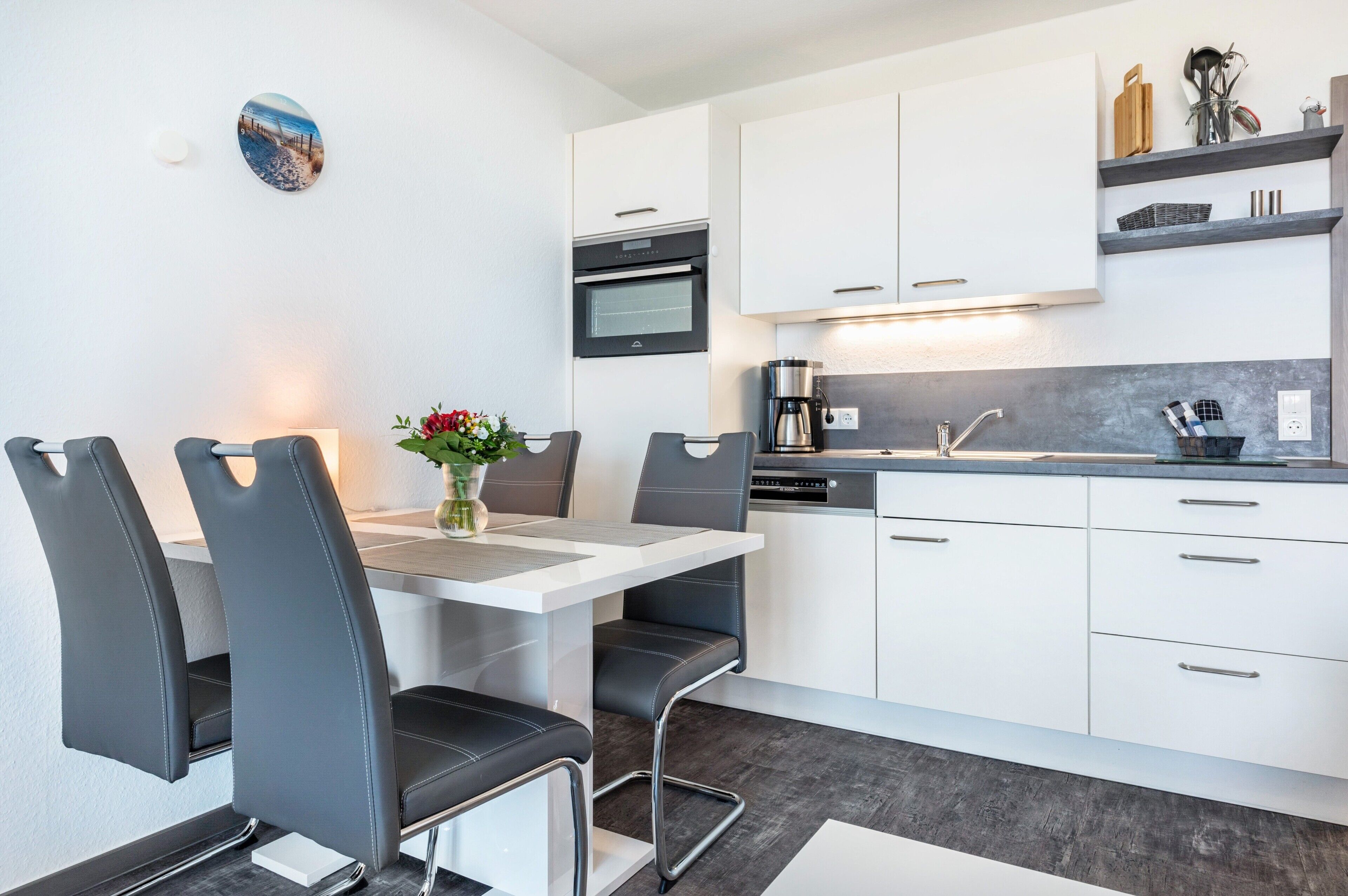 A modern kitchen with white cabinets, a built-in oven, and a coffee maker.