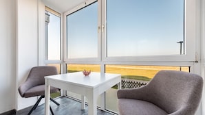 A balcony with a white table and two chairs, a clear view of the countryside, and a white wall.