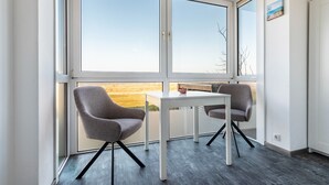 A modern room with a large window, two grey chairs, a white table, and a small painting on the wall.