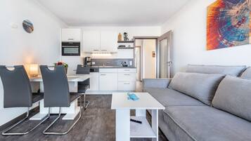 Een moderne keuken met witte kasten, een eethoek met zwarte stoelen en een grijze bank.