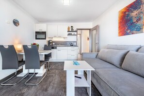 A modern kitchen with white cabinets, a dining area with black chairs, and a grey sofa. - Apartment 'Hochparterre' with Sea View, Balcony and Wi-Fi (Cuxhaven)