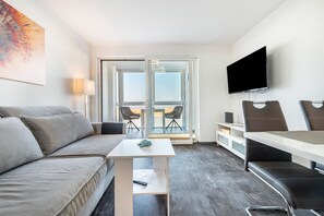 A modern hotel room with a sofa, a small table, a TV, and a balcony with chairs. - Apartment 'Hochparterre' with Sea View, Balcony and Wi-Fi (Cuxhaven)