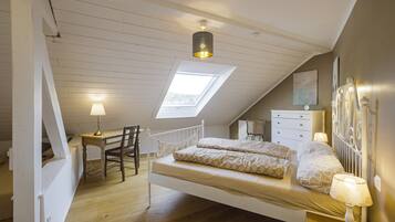 Een slaapkamer met een schuine kap, dakraam, bed met gestreept beddengoed, nachtkastje met lamp, stoel en een dressoir.