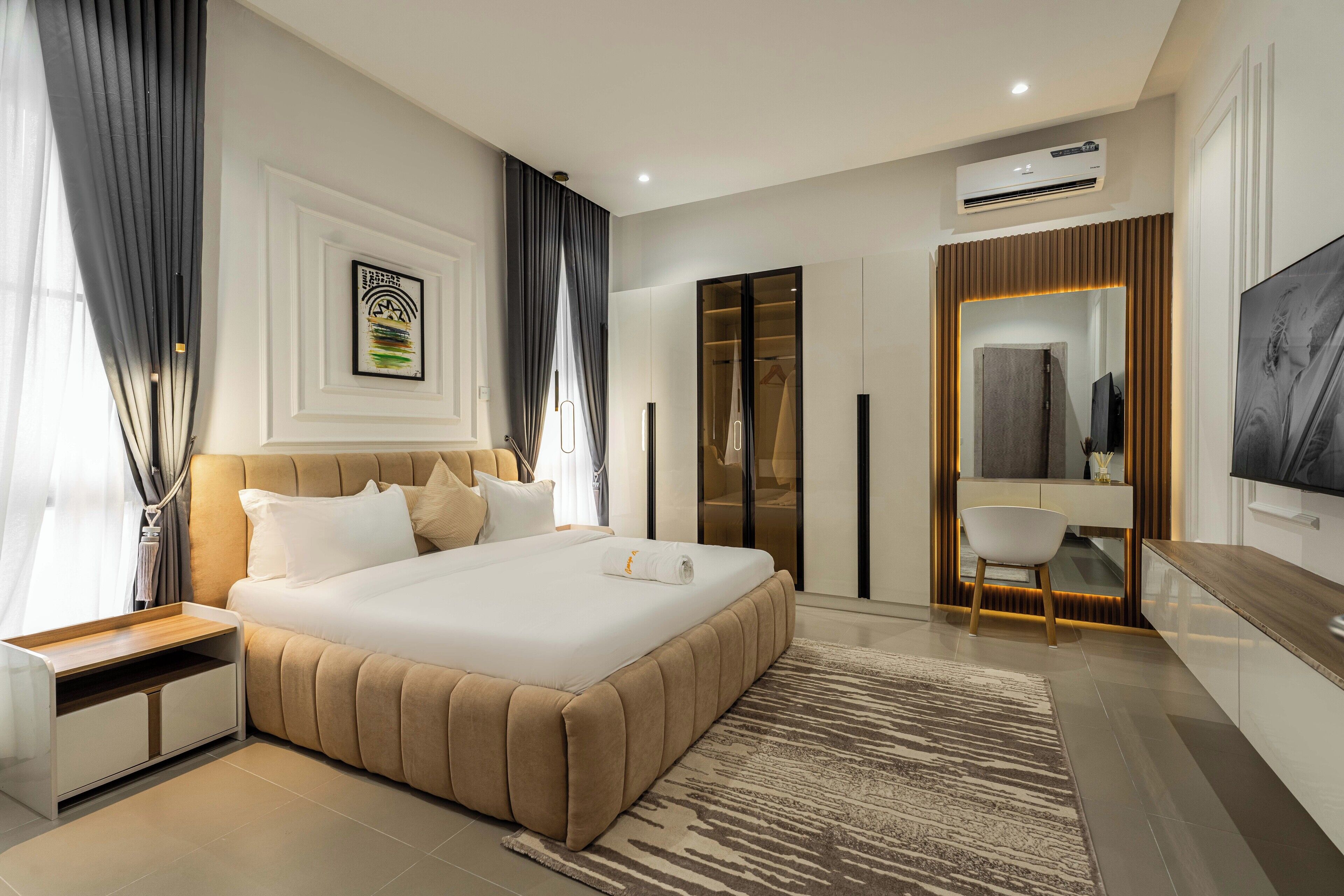 A modern hotel bedroom with a large bed, a desk, a chair, and a TV.