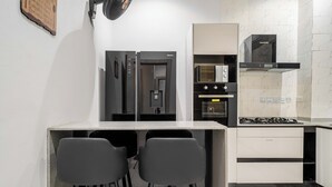 Une cuisine compacte équipée d’un réfrigérateur, d’un four, d’un four à micro-ondes et d’une cuisinière à gaz. Elle comprend deux tabourets de bar et un petit comptoir.