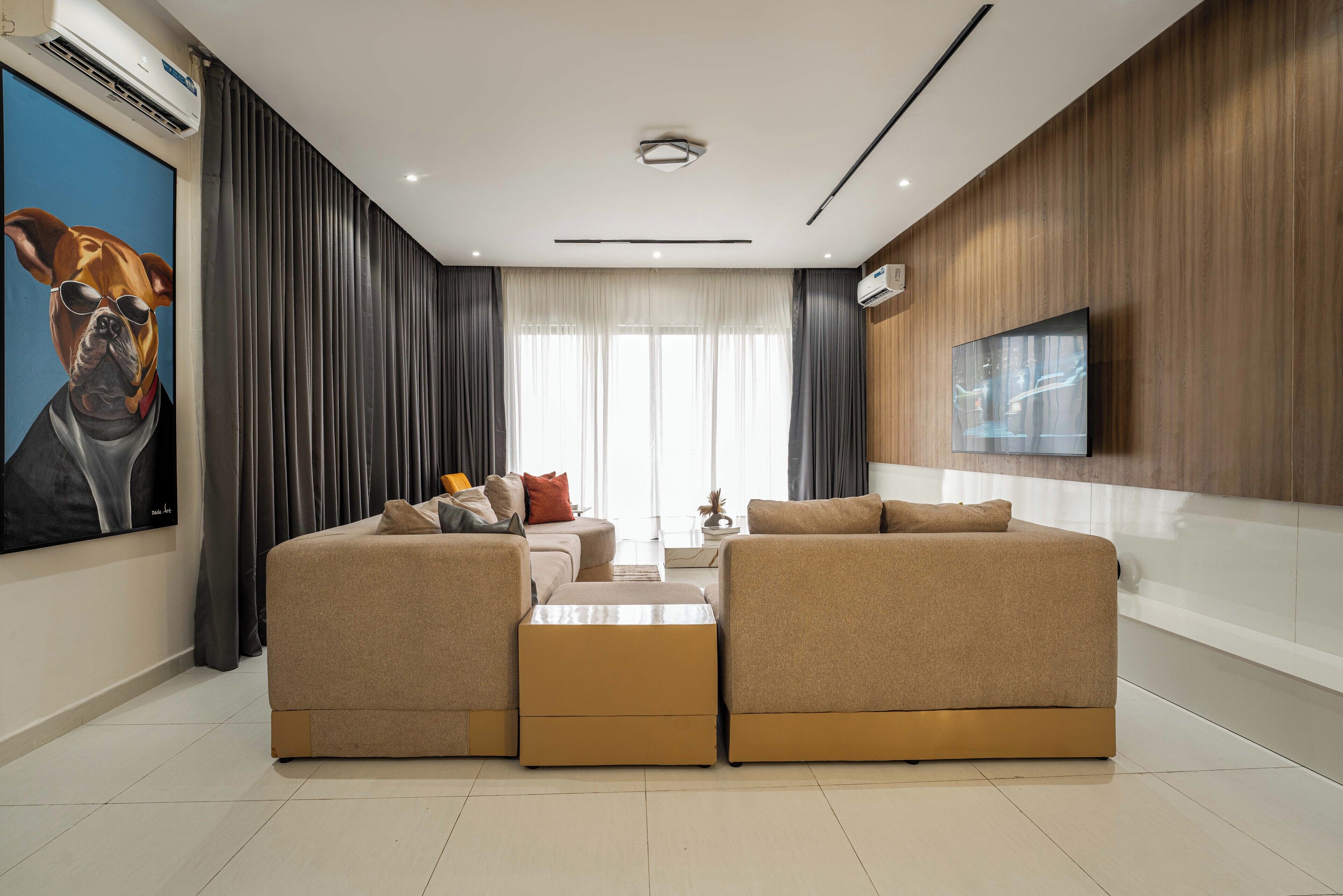 A modern living room with a sectional sofa, a coffee table, and a flat-screen TV mounted on the wall.