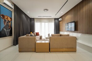 A modern living room with a sectional sofa, a coffee table, and a flat-screen TV mounted on the wall. - George Residence Lekki Phase 1 (Lekki)