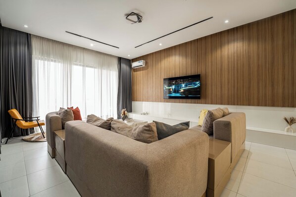 A modern living room with a sectional sofa, a coffee table, and a flat-screen TV mounted on a wooden wall. - George Residence Lekki Phase 1 (Lekki)