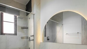 Une salle de bain moderne dotée d’une douche à parois de verre, de toilettes, d’un lavabo et d’un miroir au design en forme d’arc.