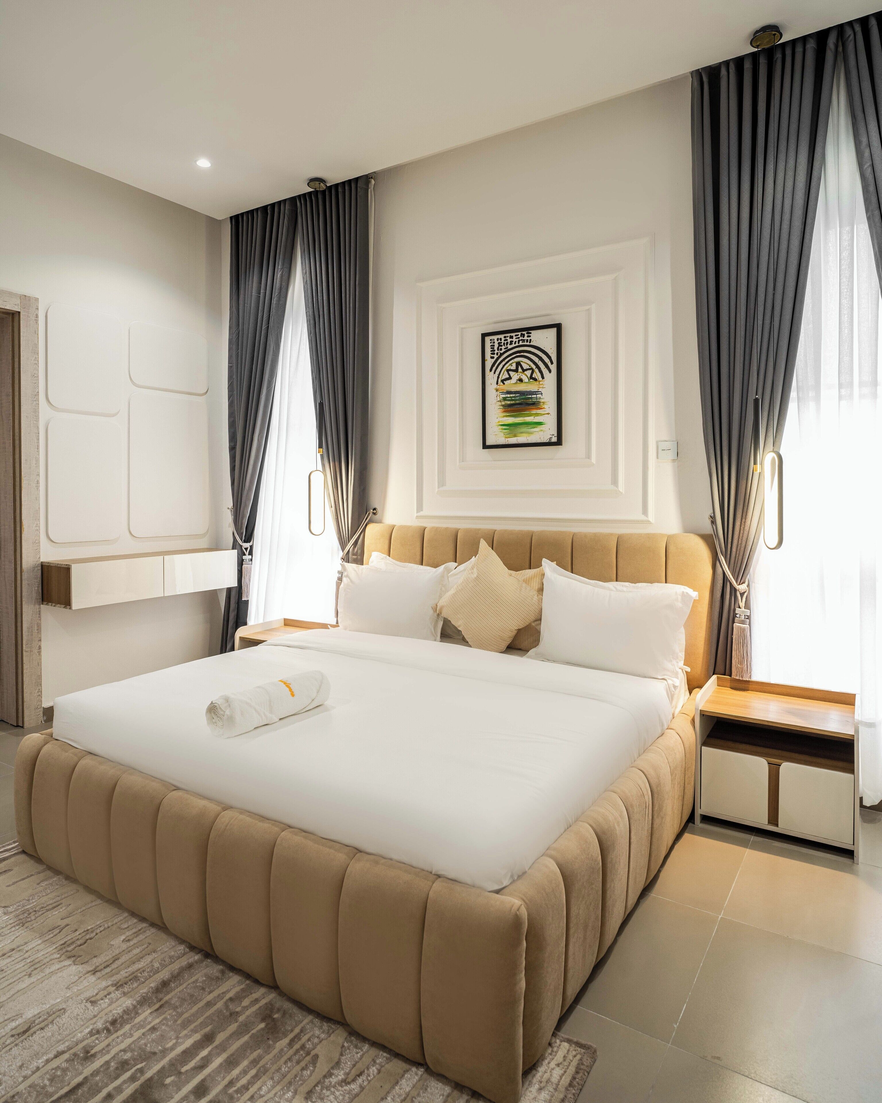 A modern hotel room with a large bed, a bedside table, a wall-mounted TV, and a framed artwork above the bed.