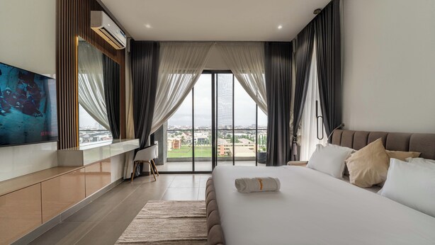 Une chambre d’hôtel moderne dotée d’un grand lit, d’un téléviseur fixé au mur et offrant une vue sur la ville grâce à de grandes fenêtres.