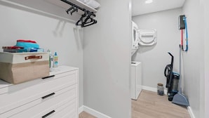 A clean, modern bathroom with a white vanity, a towel rack, a vacuum cleaner, and a white toilet.