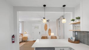 A modern kitchen with white cabinetry, a dishwasher, and a dining area with wicker chairs.