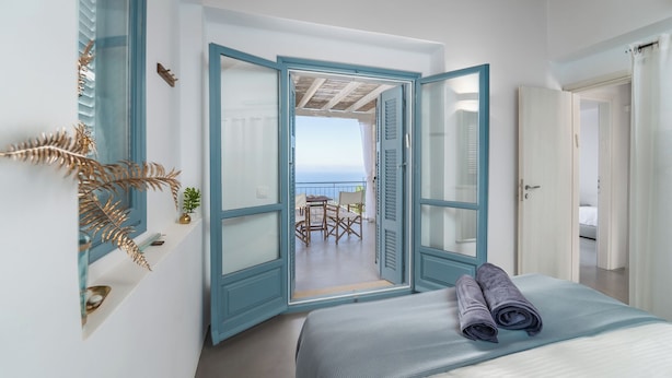 A bedroom with a bed, a view of the sea through an open door, and a balcony with chairs. - Villa Etoni, stunning sea views, infinity pool and privacy (Kalamitsi)