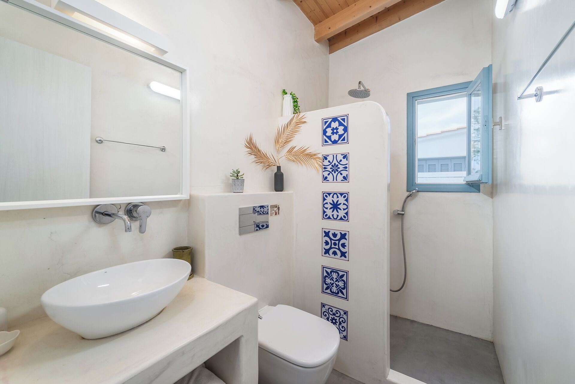 Une salle de bain avec un lavabo blanc, des toilettes, une douche avec une fenêtre et des carreaux décoratifs.