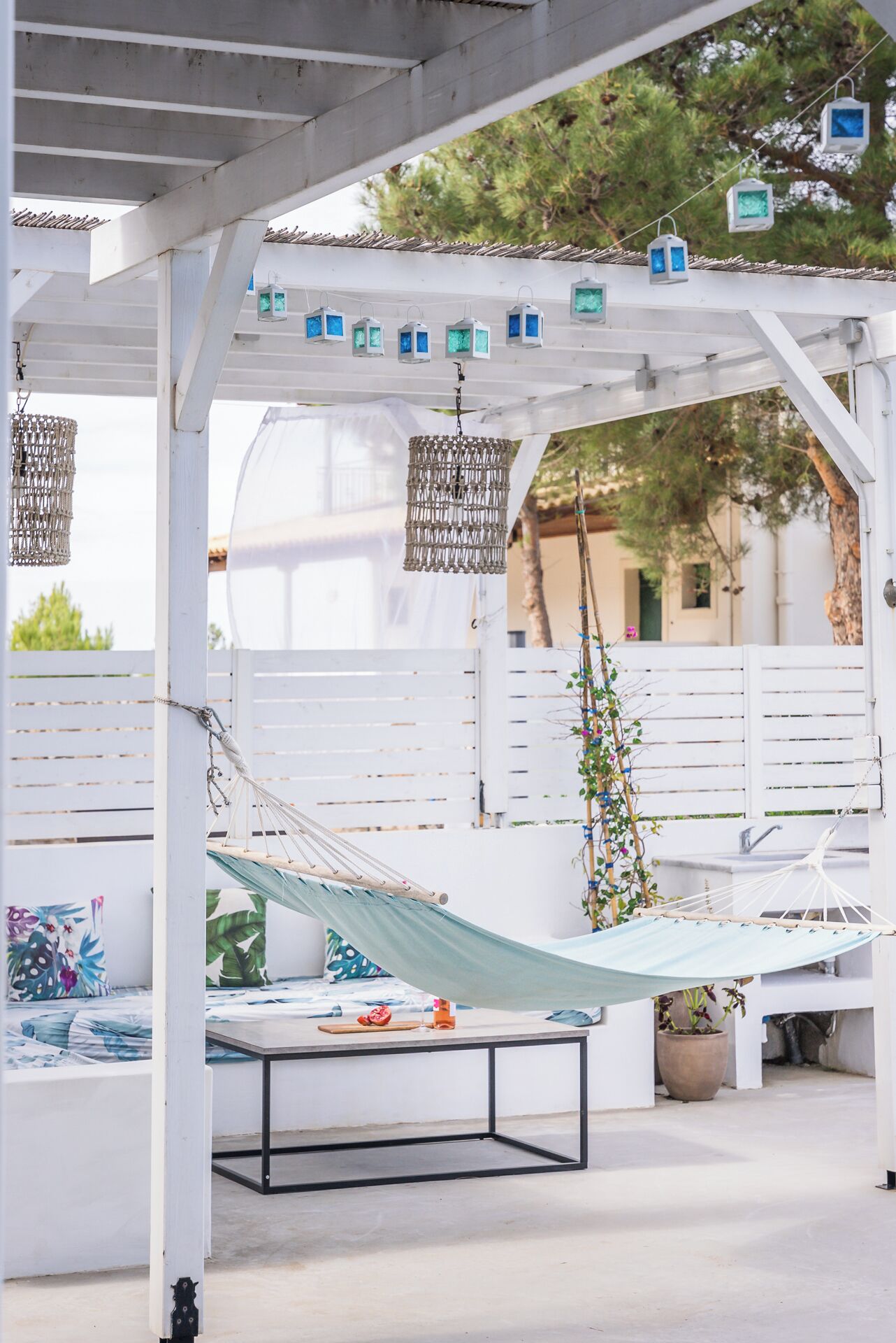A covered outdoor seating area with two hammocks, a white pergola, and hanging lanterns.
