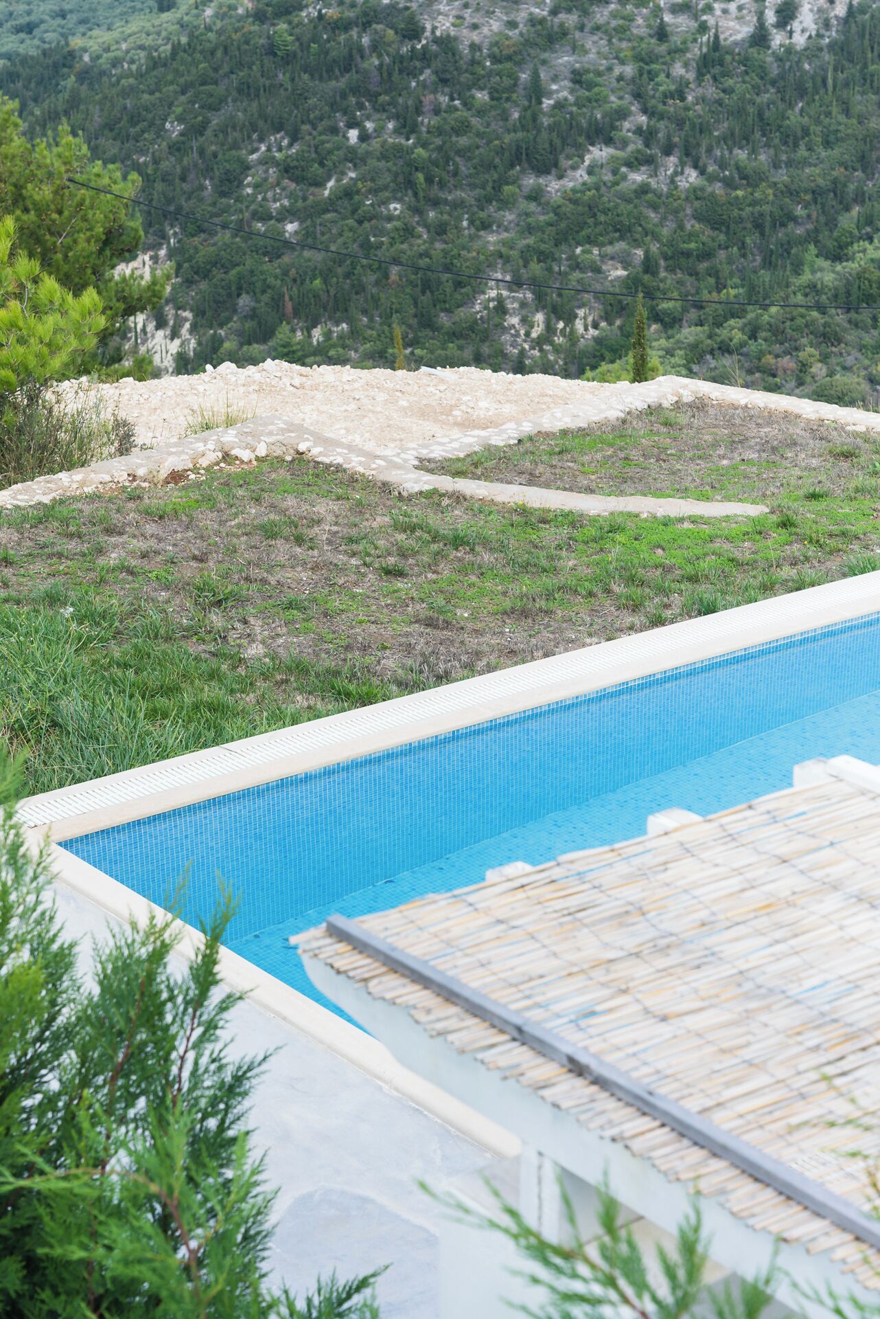 A swimming pool with a tiled edge, surrounded by grass and trees.