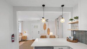 A modern kitchen with white cabinetry, a dishwasher, and a dining area with wicker chairs.