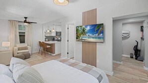 A hotel room with a bed, a desk, a kitchenette, and a painting of a beach scene.